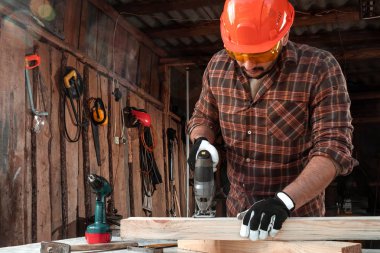 Bir marangoz elektrikli bir yapboz ile tahta bir kirişi keser, erkek eli elektrikli bir yapboz ile yakın plan. Tahtayla çalış.