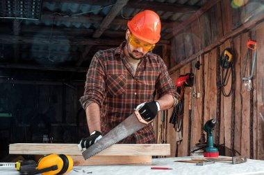 Bir marangoz ahşap bir kirişi el testeresiyle keser, erkek eli testereyle yakın plan çekilir. Tahtayla çalış.