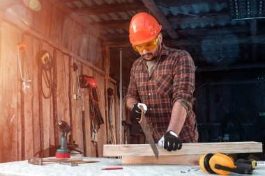 Bir marangoz ahşap bir kirişi el testeresiyle keser, erkek eli testereyle yakın plan çekilir. Tahtayla çalış.