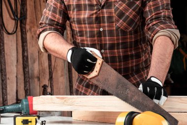 Bir marangoz ahşap bir kirişi el testeresiyle keser, erkek eli testereyle yakın plan çekilir. Tahtayla çalış.