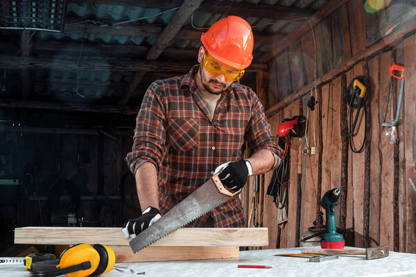 A man carpenter cuts a wooden beam using a handsaw, male hands with a saw closeup. Work with wood.