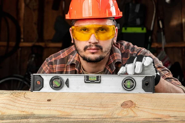 Builder man kijkt naar het bouwniveau controleert het horizontale oppervlak, mannelijke handen met een level close-up. Bouwwerkzaamheden, reparatie. — Stockfoto