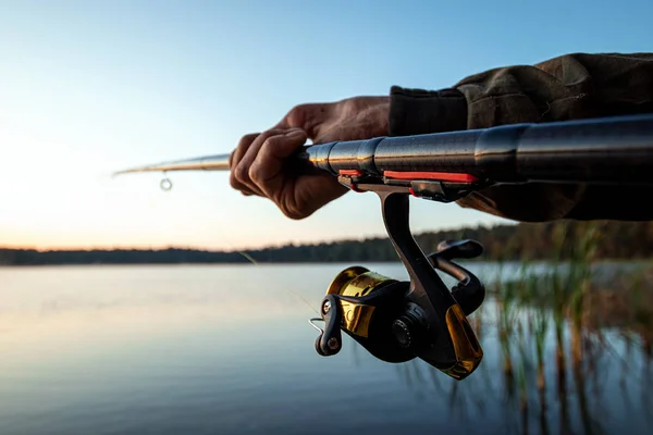 Las manos de un hombre en un plan Urp sostienen una caña de pescar, un pescador captura peces al amanecer. Pesca hobby concepto de vacaciones. Copiar espacio . —  Fotos de Stock