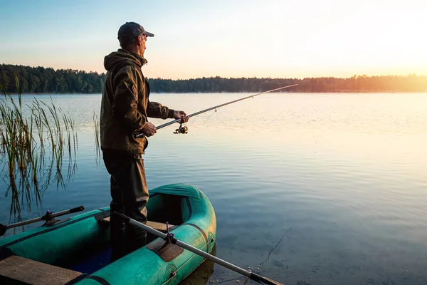 Homem pescador ao amanhecer no lago pega uma vara de pesca. Conceito de férias hobby de pesca. Espaço de cópia . — Fotografia de Stock