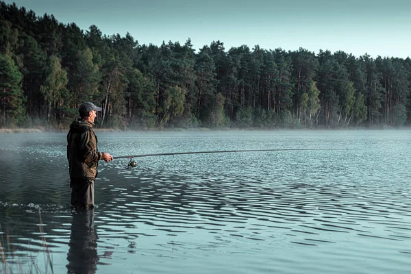 Un pescador macho en el lago está parado en el agua y pescando una caña de pescar. Pesca hobby concepto de vacaciones. Copiar espacio. — Foto de Stock
