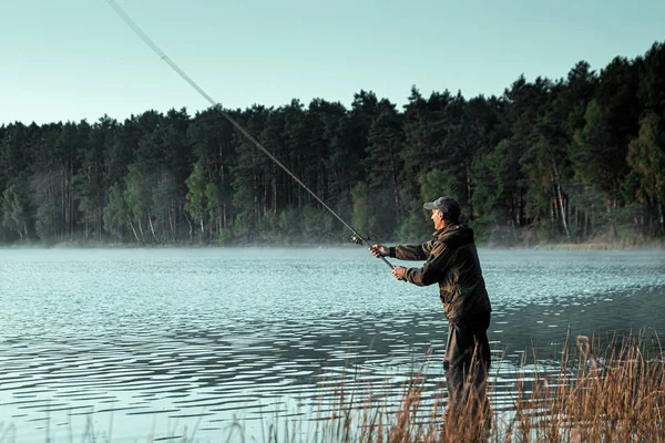 Een mannelijke visser op het meer staat in het water te vissen op een hengel. Vissen hobby vakantie concept. Kopieerruimte. — Stockfoto
