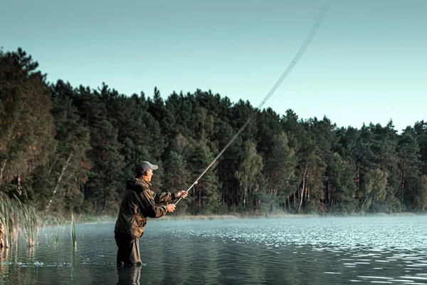 Ein männlicher Fischer am See steht im Wasser und angelt nach einer Angel. Angeln Hobby Urlaubskonzept. Kopierraum. — Stockfoto