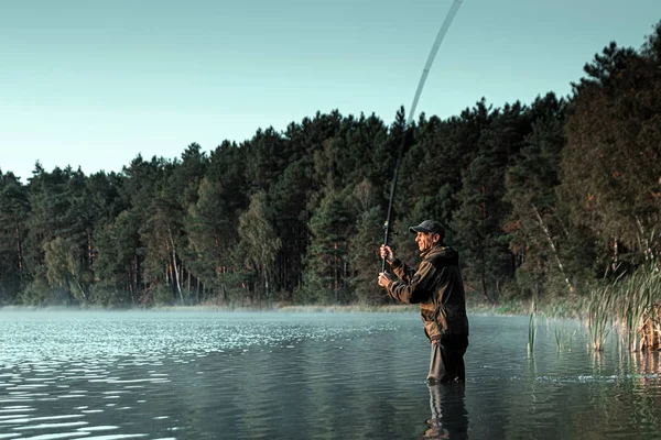 Ένας αρσενικός ψαράς στη λίμνη στέκεται στο νερό και ψαρεύει καλάμι. Ψάρεμα χόμπι διακοπές έννοια. Αντιγραφή χώρου. — Φωτογραφία Αρχείου
