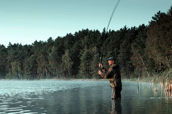 Un pescatore maschio sul lago è in piedi in acqua e la pesca di una canna da pesca. Pesca concetto di vacanza hobby. Copia spazio. — Foto Stock