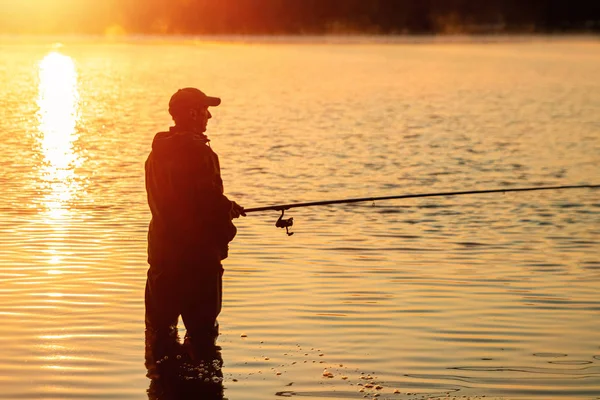 Pescatore maschio all'alba sul lago cattura una canna da pesca. Pesca concetto di vacanza hobby. Copia spazio . — Foto Stock