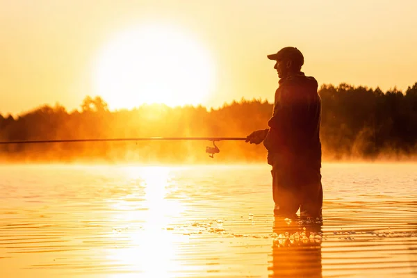 Ein männlicher Fischer fängt im Morgengrauen am See eine Angelrute. Angeln Hobby Urlaubskonzept. Kopierraum. — Stockfoto