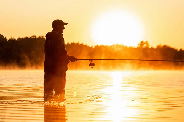 Ein männlicher Fischer fängt im Morgengrauen am See eine Angelrute. Angeln Hobby Urlaubskonzept. Kopierraum. — Stockfoto