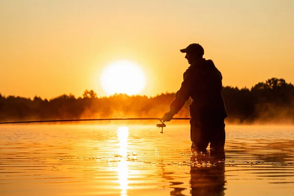 Ein männlicher Fischer fängt im Morgengrauen am See eine Angelrute. Angeln Hobby Urlaubskonzept. Kopierraum. — Stockfoto