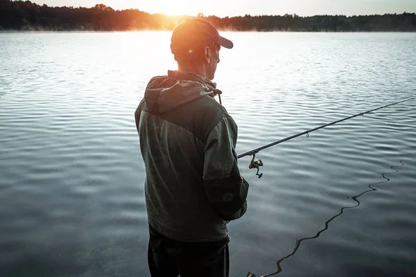 Ein männlicher Fischer am See steht im Wasser und angelt nach einer Angel. Angeln Hobby Urlaubskonzept. Kopierraum. — Stockfoto