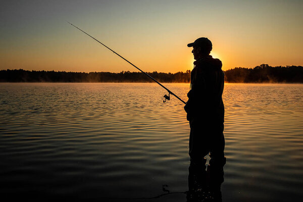 Мужчина рыбак на рассвете на озере ловит удочку. Концепция отдыха на лодке. Копирование пространства
.