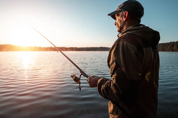 Homem pescador ao amanhecer no lago pega uma vara de pesca. Conceito de férias hobby de pesca. Espaço de cópia . — Fotografia de Stock