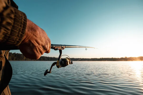 Las manos de un hombre en un plan Urp sostienen una caña de pescar, un pescador captura peces al amanecer. Pesca hobby concepto de vacaciones. Copiar espacio . — Foto de Stock