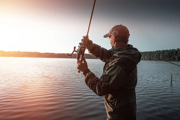 Pescatore maschio all'alba sul lago cattura una canna da pesca. Pesca concetto di vacanza hobby. Copia spazio . — Foto Stock