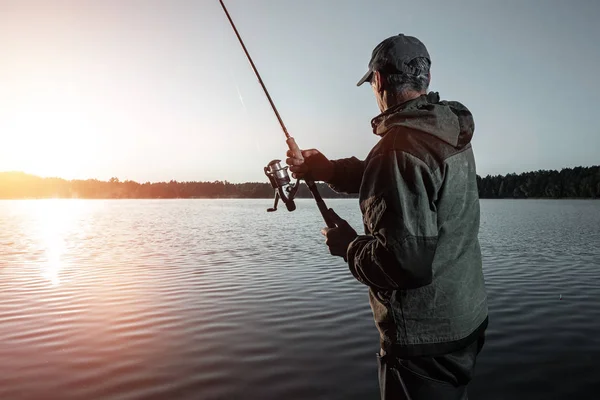 Pescatore maschio all'alba sul lago cattura una canna da pesca. Pesca concetto di vacanza hobby. Copia spazio . — Foto Stock