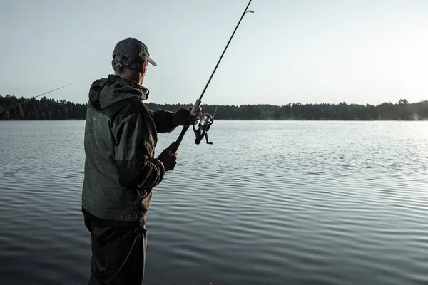 Homem pescador ao amanhecer no lago pega uma vara de pesca. Conceito de férias hobby de pesca. Espaço de cópia . — Fotografia de Stock