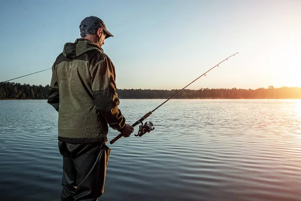 Pescatore maschio all'alba sul lago cattura una canna da pesca. Pesca concetto di vacanza hobby. Copia spazio . — Foto Stock