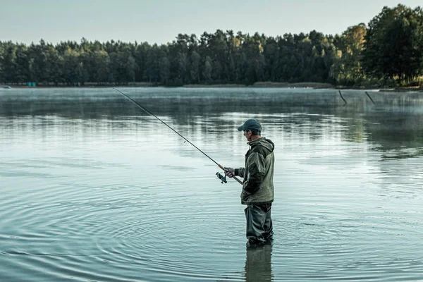 Un pescador macho en el lago está parado en el agua y pescando una caña de pescar. Pesca hobby concepto de vacaciones. Copiar espacio. —  Fotos de Stock