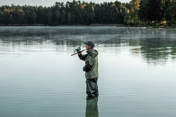 Egy férfi halász a tavon áll a vízben és horgászbotot keres. Horgász hobbi nyaralás koncepció. Fénymásolási hely. — Stock Fotó