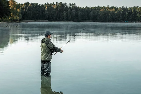 Um pescador masculino no lago está de pé na água e pescando por uma vara de pesca. Conceito de férias hobby de pesca. Espaço de cópia. — Fotografia de Stock