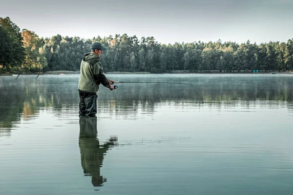 Egy férfi halász a tavon áll a vízben és horgászbotot keres. Horgász hobbi nyaralás koncepció. Fénymásolási hely. — Stock Fotó