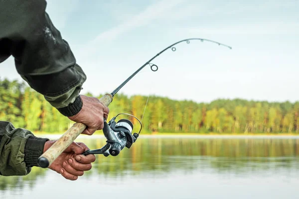 Las manos de un hombre en un plan Urp sostienen una caña de pescar, un pescador captura peces al amanecer. Pesca hobby concepto de vacaciones. Copiar espacio . —  Fotos de Stock