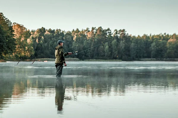 Um pescador masculino no lago está de pé na água e pescando por uma vara de pesca. Conceito de férias hobby de pesca. Espaço de cópia. — Fotografia de Stock