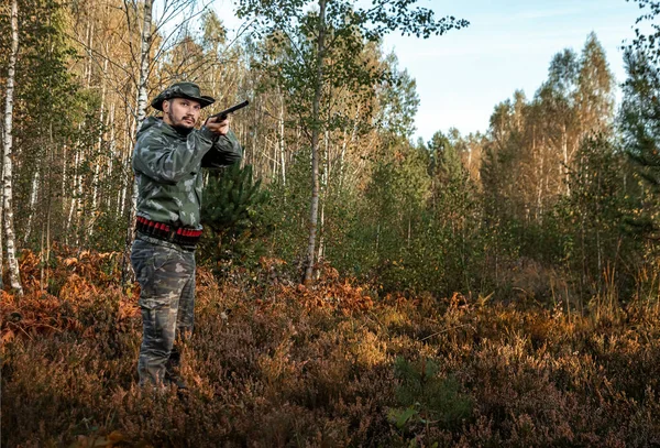 Homem caçador em camuflagem com uma arma durante a caça em busca de pássaros selvagens ou jogo no fundo da floresta de outono. Temporada de caça de outono. O conceito de um hobby, matando . — Fotografia de Stock