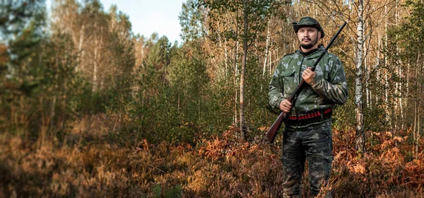 Lovec muž v maskování s pistolí během lovu při hledání volně žijících ptáků nebo zvěře na pozadí podzimního lesa. Podzimní lovecká sezóna. Koncept koníčku, zabíjení. — Stock fotografie
