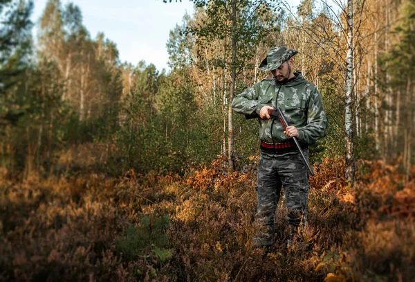 Lovec muž v maskování s pistolí během lovu při hledání volně žijících ptáků nebo zvěře na pozadí podzimního lesa. Podzimní lovecká sezóna. Koncept koníčku, zabíjení. — Stock fotografie