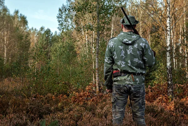 Homem caçador em camuflagem com uma arma durante a caça em busca de pássaros selvagens ou jogo no fundo da floresta de outono. Temporada de caça de outono. O conceito de um hobby, matando . — Fotografia de Stock