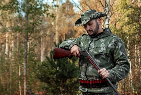 Homem caçador em camuflagem com uma arma durante a caça em busca de pássaros selvagens ou jogo no fundo da floresta de outono. Temporada de caça de outono. O conceito de um hobby, matando . — Fotografia de Stock