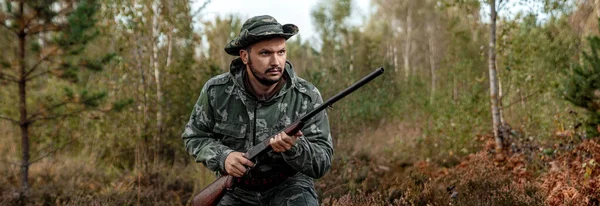 Homem caçador em camuflagem com uma arma durante a caça em busca de pássaros selvagens ou jogo no fundo da floresta de outono. Temporada de caça de outono. O conceito de um hobby, matando . — Fotografia de Stock