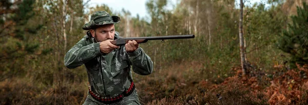 Homem caçador em camuflagem com uma arma durante a caça em busca de pássaros selvagens ou jogo no fundo da floresta de outono. Temporada de caça de outono. O conceito de um hobby, matando . — Fotografia de Stock