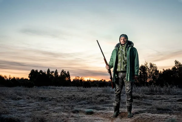 Jäger Mann in Tarnung mit einem Gewehr während der Jagd auf der Suche nach Wildvögeln oder Wild auf einem schönen Sonnenuntergang. das Konzept eines Hobbys, des Tötens. — Stockfoto