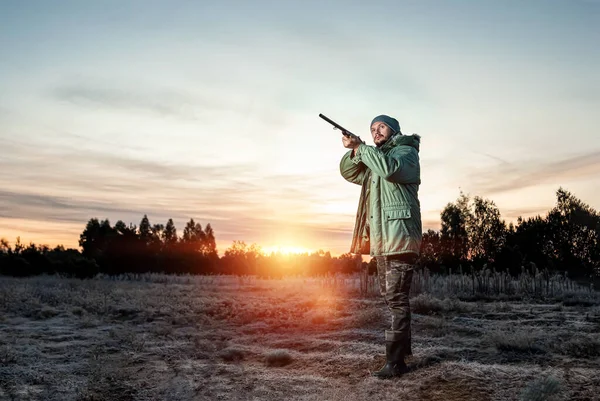 Lovec muž v maskování s pistolí během lovu při hledání volně žijících ptáků nebo zvěře na krásném západu slunce. Koncept koníčku, zabíjení. — Stock fotografie