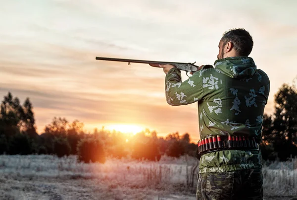 Lovec muž v maskování s pistolí během lovu při hledání volně žijících ptáků nebo zvěře na krásném západu slunce. Koncept koníčku, zabíjení. — Stock fotografie