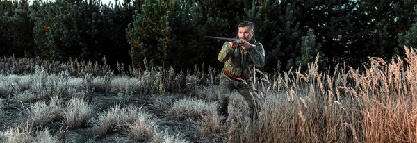 Homem caçador em camuflagem com uma arma durante a caça em busca de pássaros selvagens ou jogo no fundo da floresta de outono. Temporada de caça de outono. O conceito de um hobby, matando . — Fotografia de Stock