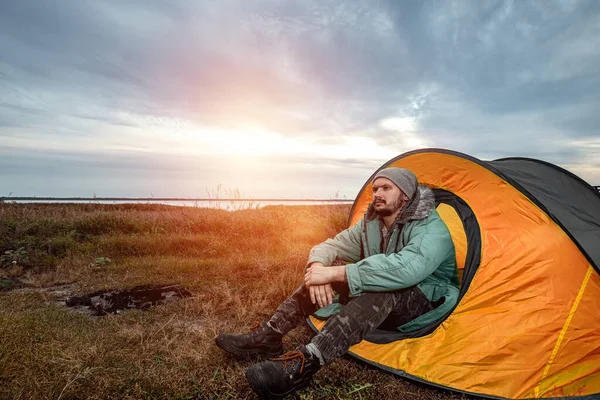 Un barbu campe dans une tente sur fond de nature et de lac. Le concept de voyage, tourisme, camping . — Photo