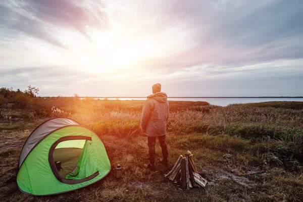 Brodaty mężczyzna w pobliżu namiotu kempingowego w zieleni na tle natury i jeziora. Koncepcja podróży, turystyki, kempingu. — Zdjęcie stockowe