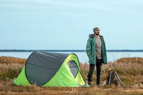 Бородатый мужчина возле палатки в зеленом на фоне природы и озера. Концепция путешествий, туризма, кемпинга . — стоковое фото