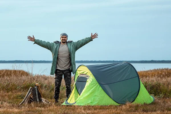 Vousatý muž v zeleném stanu na pozadí přírody a jezera. Koncept cestování, cestovního ruchu, kempování. — Stock fotografie