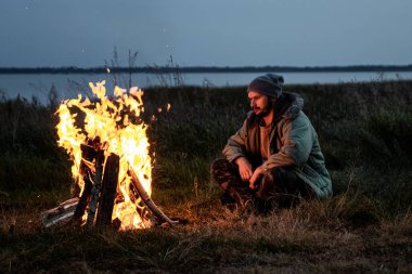 Kamp yapan adam gece ateşin başında gökyüzüne karşı oturuyor. Seyahat, turizm, kamp konsepti.