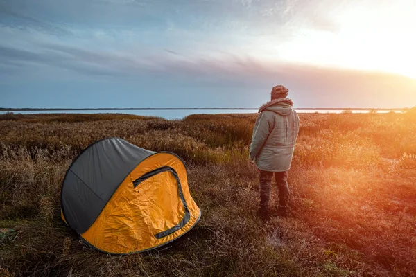 Ein bärtiger Mann in der Nähe eines Zeltes in Orange vor dem Hintergrund der Natur und des Sees. das Konzept von Reisen, Tourismus, Zelten. — Stockfoto