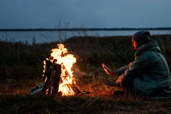 Zeltmann, der nachts am Feuer gegen den Himmel sitzt. das Konzept von Reisen, Tourismus, Zelten. — Stockfoto