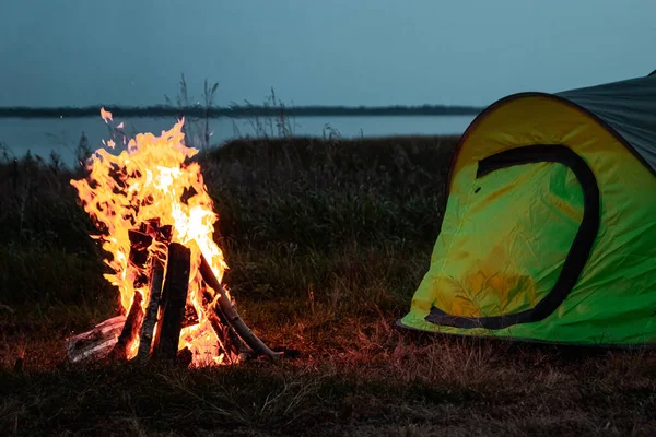 El acampante se sienta junto al fuego por la noche contra el fondo del cielo estrellado. El concepto de viajes, turismo, camping . —  Fotos de Stock